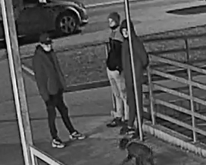 zdjęcie czarno-białe: trzech mężczyzn ubranych w ciemne kurtki i spodnie z maseczkami na twarzy stojących na chodniku, w rejonie podjazdu