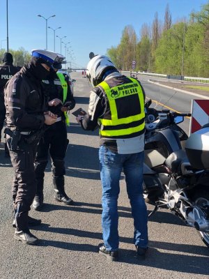 zdjęcie kolorowe: dwóch policjantów katowickiej drogówki podczas rozmowy z kierującym motocyklem
