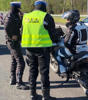 zdjęcie kolorowe: dwóch policjantów katowickiej drogówki  podczas kontroli drogowej podjętej wobec motocyklisty