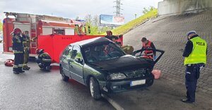 zdjęcie kolorowe: policjant katowickiej drogówki, zespół ratownictwa medycznego i strażacy wykonujący czynności na miejscu zdarzenia drogowego