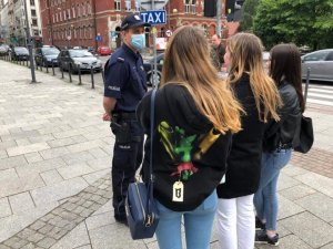 zdjęcie kolorowe: policjant rozmawiający z trzema nastolatkami na temat przepisów dotyczących telefonów komórkowych