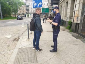zdjęcie kolorowe: policjant rozmawiający z młodym mężczyzna w rejonie oznakowanego przejścia dla pieszych