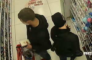 zdjęcie kolorowe: dwóch mężczyzn ubranych na czarno w drogerii stojących do siebie plecami z maseczkami ochronnymi na twarzy