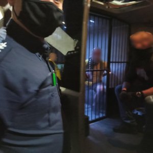 zdjęcie kolorowe: zatrzymany pseudokibic w towarzystwie dwóch policjantów w samochodzie do przewożenia osób zatrzymanych