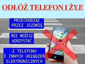 zdjęcie kolorowe: plakat promujący akcję "Odłóż telefon i żyj" przedstawiający na tle przejścia dla pieszych telefon komórkowy trzymany w dłoni. Poniżej obowiązujące przepisy prawa w tym zakresie