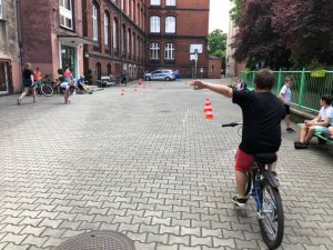 zdjęcie kolorowe: chłopiec na rowerze sygnalizujący manewr skrętu w lewo podczas egzaminu na kartę rowerową