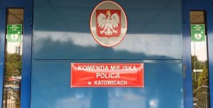 zdjęcie kolorowe: wejście główne do budynku Komendy Miejskiej Policji w Katowicach z informacją, że w budynku znajduje si e AED