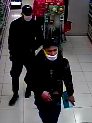 zdjęcie kolorowe: dwóch mężczyzn ubranych w czarne ubrania z czapeczkami na głowie i maseczkami ochronnymi na twarzy przechadzający się po sklepie kosmetycznym