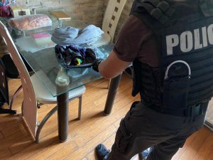 zdjęcie kolorowe: policjant przeszukujący torebkę tzw. nerkę na stole w pokoju
