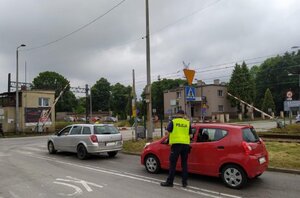 zdjęcie kolorowe: policjant katowickiej komendy rozmawia z kierującym samochodem osobowym przed zamkniętym przejazdem kolejowym