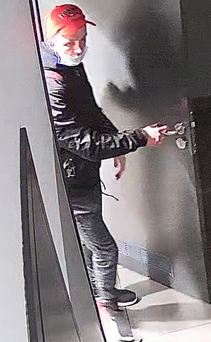 zdjęcie kolorowe: mężczyzna wychodzący z toalety ubrany w czerwona czapkę z daszkiem, czarne buty sportowe z czerwono-biała podeszwą, ciemnoszare spodnie, czarna kurtkę, maseczkę ochronna na twarzy i bordowy plecak na ramieniu