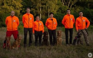 zdjęcie kolorowe: strażacy - ochotnicy ze swoimi psami służbowymi stojący na polanie