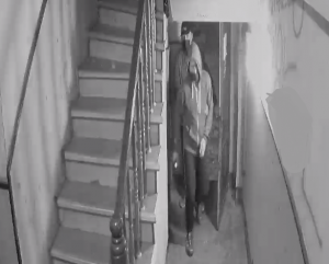 zdjęcie czarno-białe: dwóch zamaskowanych mężczyzn wchodzących do klatki schodowej