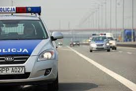 zdjęcie kolorowe: policyjny radiowóz na tle drogi wielopasmowej i jadących samochodów