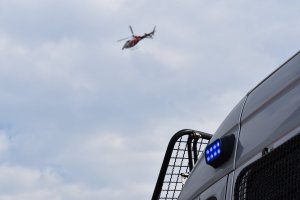 Zdjęcie kolorowe przedstawia niebieskie światło błyskowe radiowozu policyjnego, a w tle lecący helikopter.