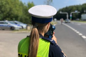 Zdjęcie kolorowe przedstawia policjantkę Wydziału Ruchu Drogowego podczas pomiaru prędkości pojazdu.
