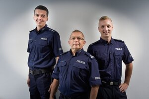 zdjęcie kolorowe: trzech policjantów w umundurowaniu służbowych stojących na tle szarej ściany