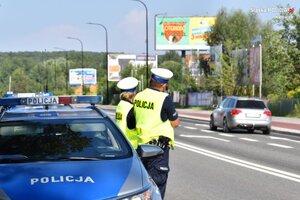 zdjęcie kolorowe: policjanci katowickiej drogówki stojący przed radiowozem przy krawędzi jezdni