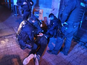 zdjęcie kolorowe: umundurowani policjanci trzymające osobę leżącą na chodniku, która chciała dokonać samookaleczenia