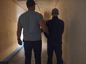 zdjęcie kolorowe: nieumundurowany policjant z zatrzymanym mężczyzną podejrzanym o fałszywy alarm na korytarzu budynku komendy