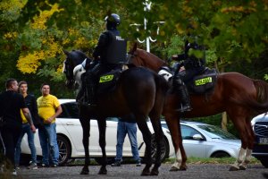 zdjęcie kolorowe: policjanci w służbie konnej nadzorujący przemarsz kibiców