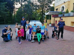 zdjęcie kolorowe: dzielnicowi z Komisariatu III Policji w Katowicach przy policyjnym radiowozie razem z dziećmi z domu dziecka