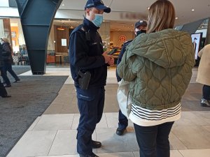 zdjęcie kolorowe: policjant  w centrum handlowym rozmawia z kobietą, która nie miała założonej maseczki na twarzy