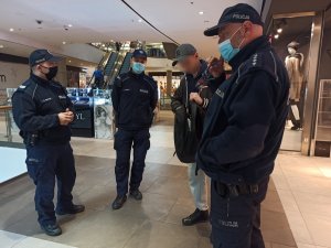 zdjęcie kolorowe: trzech umundurowanych policjantów w centrum handlowym rozmawiający z mężczyzną, który nie miał założonej maseczki na twarzy