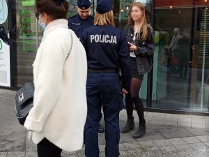 zdjęcie kolorowe: dwóch umundurowanych policjantów w centrum handlowym rozmawiający z kobieta, która nie miała założonej maseczki na twarzy w tramwaju