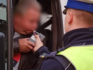 zdjęcie kolorowe: policjant przeprowadzający badanie trzeźwości kierującego busem