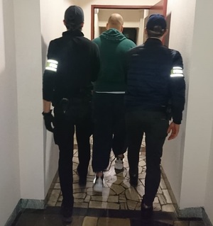 zdjęcie kolorowe: dwóch nieumundurowanych policjantów prowadzących mężczyznę podejrzanego o usiłowania zabójstwa 81-letniej kobiety