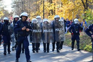 zdjęcie kolorowe: grupa policjantów oddziału prewencji maszerujący z kibicami w stronę katowickiego stadionu