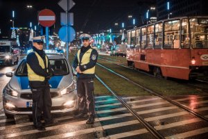 zdjęcie kolorowe: policjanci ruchu drogowego przed radiowozem w centrum Katowic obok przejeżdżającego tramwaju