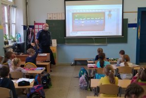 zdjęcie kolorowe: dzielnicowy stojący w klasie przy biurku podczas zajęć z uczniami klasy pierwszej