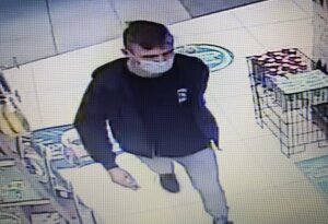 zdjęcie kolorowe: młody mężczyzna ubrany w jasne niebieskie spodnie jeansowe, czarna bluzę dresową i niebieska maseczkę ochronna założoną na twarz wchodzący do sklepu