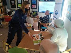 zdjęcie kolorowe: policjantka rozdająca elementy odblaskowe i ulotki seniorom na spotkaniu
