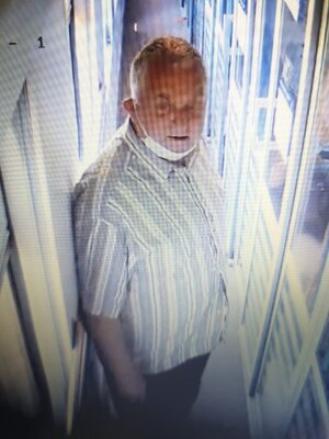 zdjęcie kolorowe: starszy mężczyzna w jasnej koszuli z siwymi włosami w przejściu wagonu z maseczka założoną pod brodą