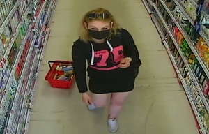 zdjęcie kolorowe: kobieta ubrana w czarna krótka sukienkę z długim rękawem i różowym napisem na piersi, z czarna maseczka ochronna na twarzy.