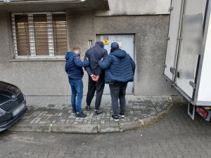 zdjęcie kolorowe: dwóch policjantów wydziału kryminalnego z zatrzymanym przed drzwiami do prokuratury