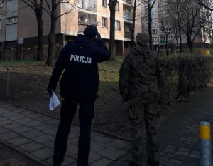 zdjęcie kolorowe: policjant i żołnierz WOT przed blokiem w centrum Katowic sprawdzają osoby objęte kwarantanną