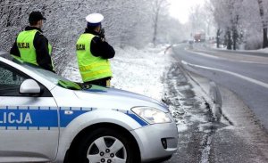 zdjęcie kolorowe: dwóch policjantów ruchu drogowego przy radiowozie kontrolujących prędkość pojazdów