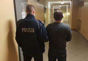 zdjęcie kolorowe: podejrzany mężczyzna z policjantem na korytarzy policyjnego aresztu