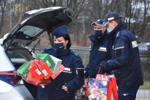 Zdjęcie kolorowe przedstawia policjantów niosących prezenty.