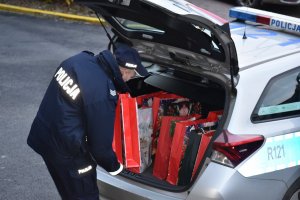 Zdjęcie kolorowe przedstawia policjanta pakującego prezenty do radiowozu.