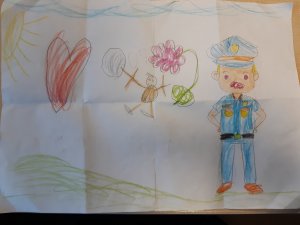 zdjęcie kolorowe: biała kartka na której narysowano policjanta, słońce, trawę, kwiatek, serce i małego ludzika oraz niebo