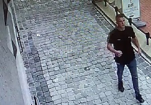 zdjęcie kolorowe: młody mężczyzna idący chodnikiem ubrany w niebieskie jeansy i czarna koszulkę z krótkim rękawem