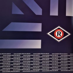 zdjęcie kolorowe: na granatowym tle gwiazdy policyjnej naniesiono znak graficzny wydziału ruchu drogowego w kształcie rombu w którym umieszczono literę R