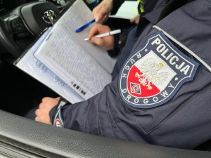 zdjęcie kolorowe: policjant wypełniający dokumentację z kontroli drogowej