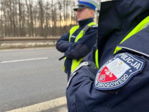 zdjęcie kolorowe: dwóch policjantów ruchu drogowego w rejonie pasa jedni, zbliżenie na naszywkę umieszczona na rękawie kurtki o treści Wydział Ruchu Drogowego, Katowice
