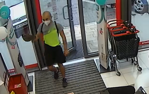 zdjęcie kolorowe: łysy młody mężczyzna w czarnych krótkich spodenkach i seledynowej koszulce z krótkim rękawem wchodzącym do sklepu kosmetycznego